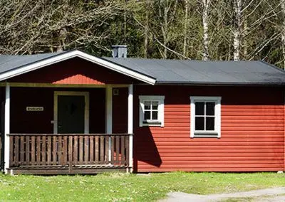 Röd stuga med veranda i skogsbrynet